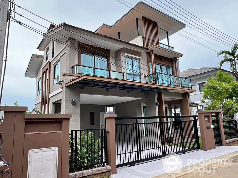 Modern two-story house with large balcony and gated entrance in suburban neighborhood.