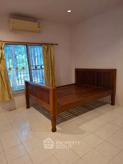 Spacious bedroom with wooden bed and tiled flooring, featuring large window with curtains.
