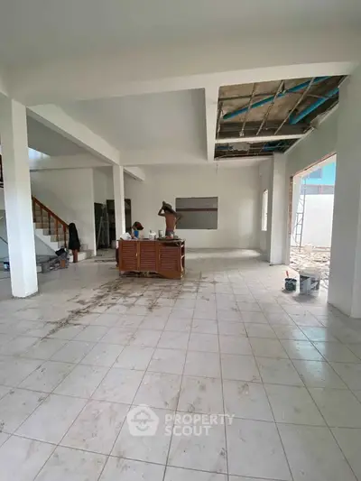 Spacious open-plan living area under renovation with tiled flooring and staircase.
