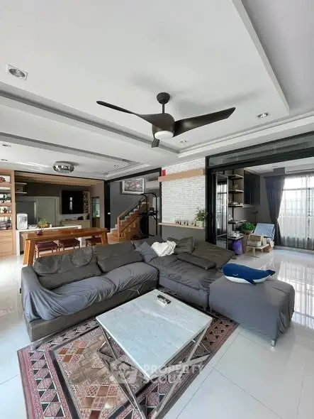 Spacious modern living room with open kitchen, featuring a large sectional sofa and stylish ceiling fan.