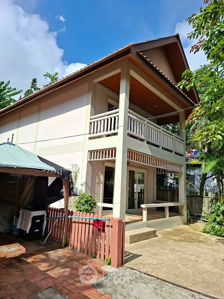 Charming two-story house with balcony and lush greenery, perfect for serene living.