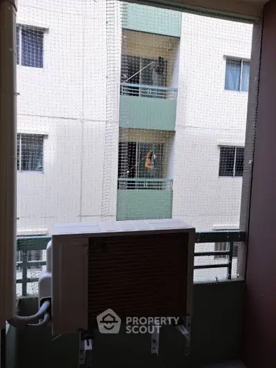 Apartment balcony with air conditioning unit and safety netting, overlooking neighboring building.