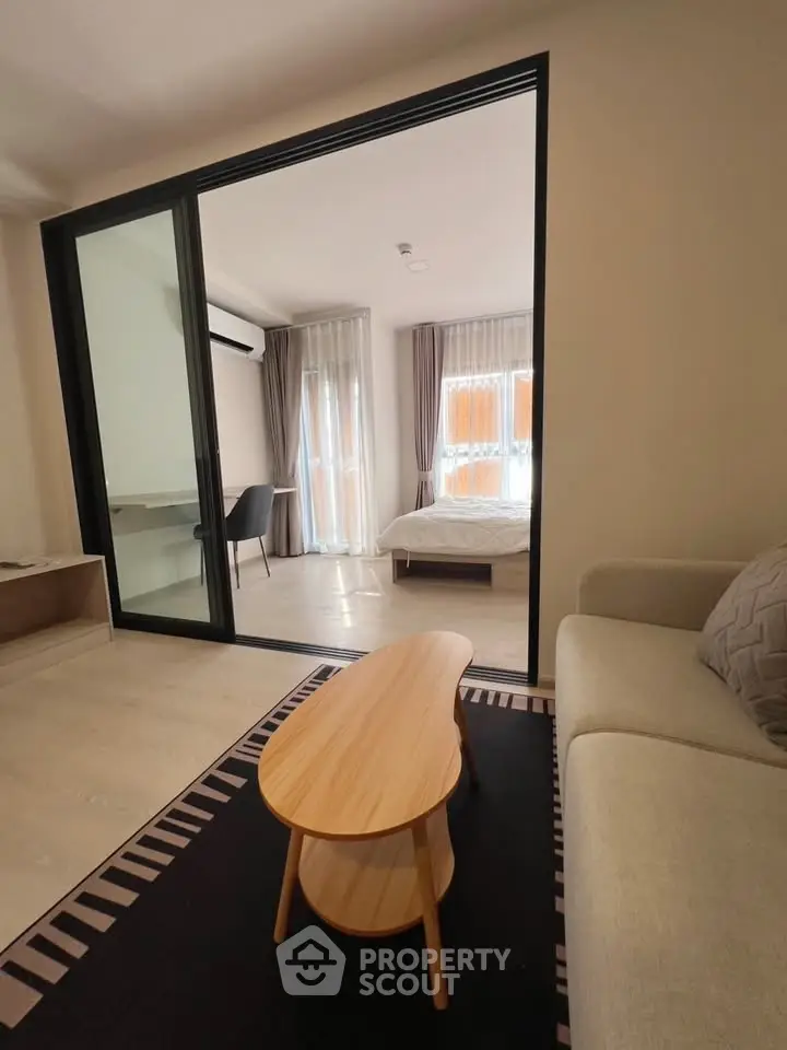 Modern living room with sliding glass doors leading to a cozy bedroom, featuring stylish furniture and natural light.