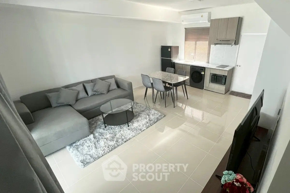 Modern living room with open kitchen, featuring sleek furniture and appliances.