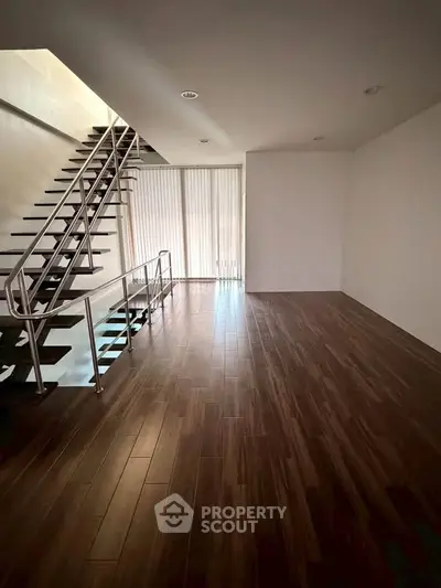 Spacious modern living room with sleek staircase and wooden flooring, perfect for contemporary living.