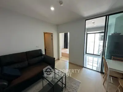 Modern living room with glass door leading to balcony, featuring sleek furniture and natural light.