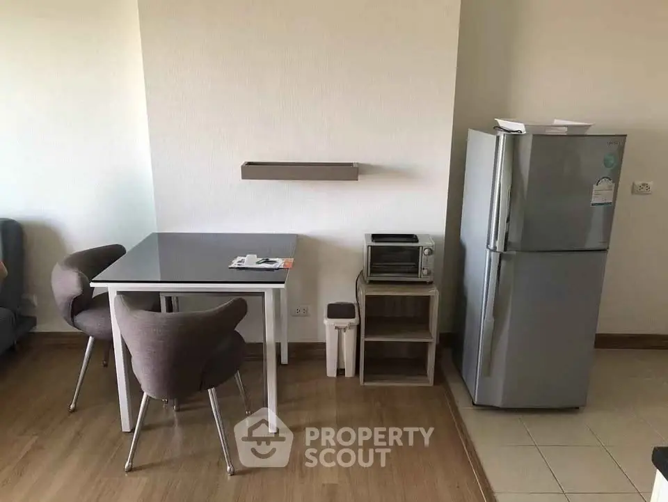 Modern kitchen corner with dining table, chairs, and stainless steel fridge in cozy apartment.