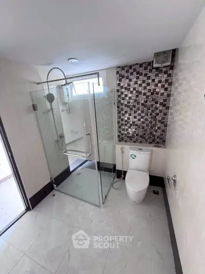 Modern bathroom with glass shower enclosure and mosaic tile accent wall.