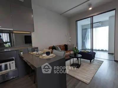 Modern open-plan living space with sleek kitchen, comfortable lounge area, and abundant natural light from large windows leading to a cozy balcony.