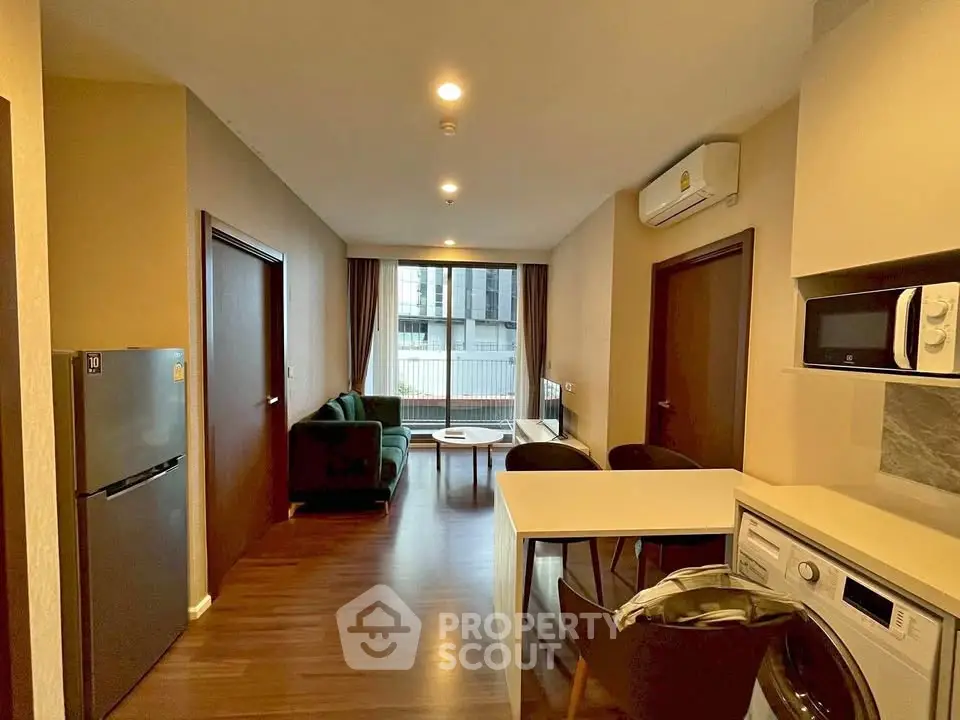 Modern living room with open kitchen, featuring washing machine and microwave, ideal for urban living.