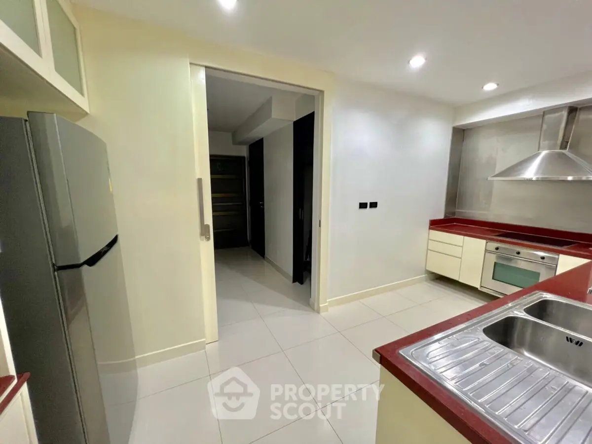 Modern kitchen with sleek design, featuring stainless steel appliances and red countertops.