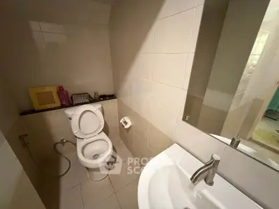 Modern bathroom with sleek fixtures and neutral tiles, featuring a toilet and sink.