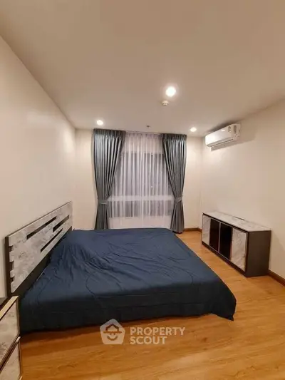 Spacious bedroom with modern decor and large window, featuring elegant curtains and wooden flooring.