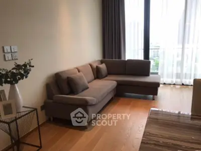 Modern living room with stylish L-shaped sofa and large window offering natural light and city view.