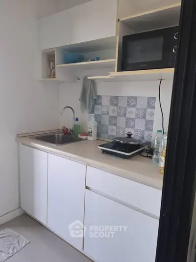Compact kitchen with modern appliances and stylish backsplash in cozy apartment.