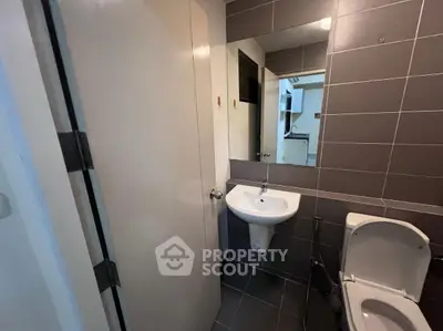 Compact bathroom with modern fixtures and tiled walls, featuring a sink and toilet.
