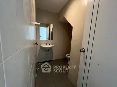 Compact bathroom with minimalist design and neutral tiles, featuring a wall-mounted sink and mirror.
