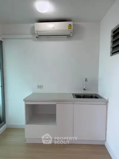 Compact kitchen with sleek white cabinetry and modern air conditioning unit.