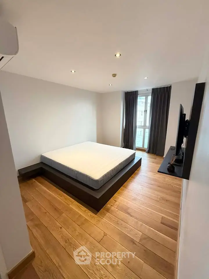 Modern minimalist bedroom with wooden flooring and large window