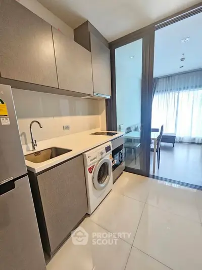 Modern kitchen with sleek cabinets, built-in washing machine, and open layout leading to dining area.