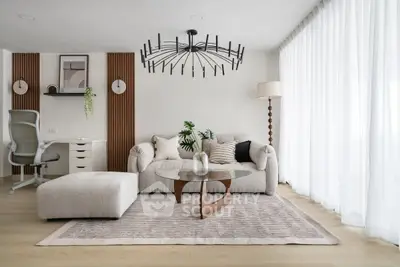 Modern living room with stylish decor, featuring a plush sofa, elegant chandelier, and natural light from large windows.