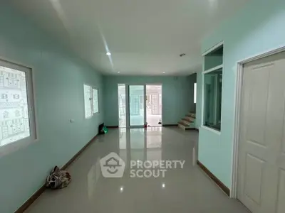 Spacious modern living room with glossy tiled floors and pastel walls, featuring large windows for natural light.