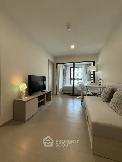 Modern living room with cozy sofa, TV, and view into a stylish bedroom with balcony access.