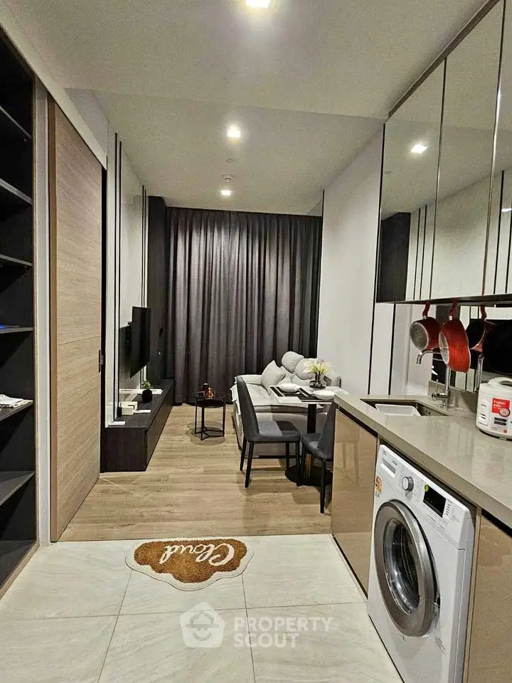 Modern open-layout living room with kitchen, featuring sleek design and integrated washing machine.