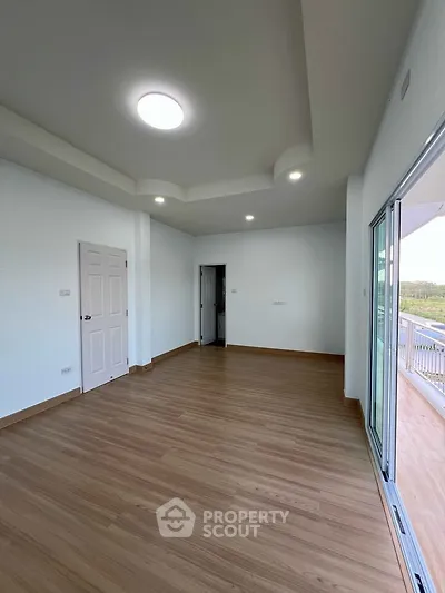 Spacious empty room with wooden flooring and balcony access in modern apartment