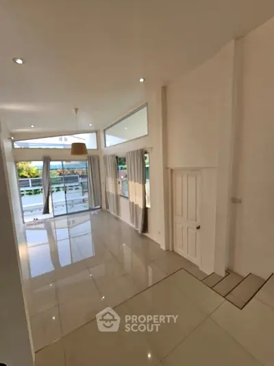 Spacious modern living room with large windows and glossy tiled floors, offering abundant natural light.