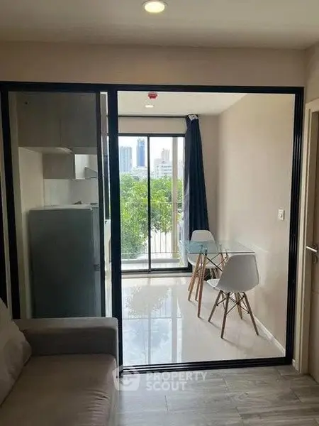 Modern apartment with glass doors leading to a balcony with city view, featuring sleek furniture and natural light.