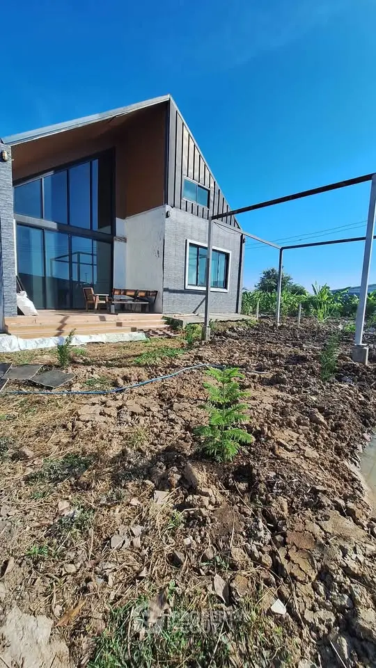 Modern architectural home with large windows and garden space under clear blue sky.
