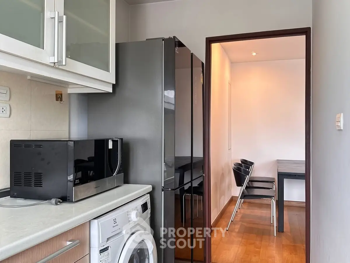 Modern kitchen with sleek appliances and adjacent dining area, featuring a washing machine and microwave.