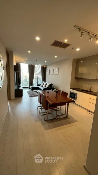 Spacious modern living room with open kitchen and dining area, featuring sleek furniture and large windows for natural light.
