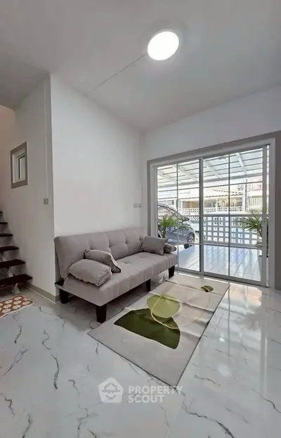 Modern living room with sleek marble flooring and cozy gray sofa, featuring large glass doors opening to a carport.