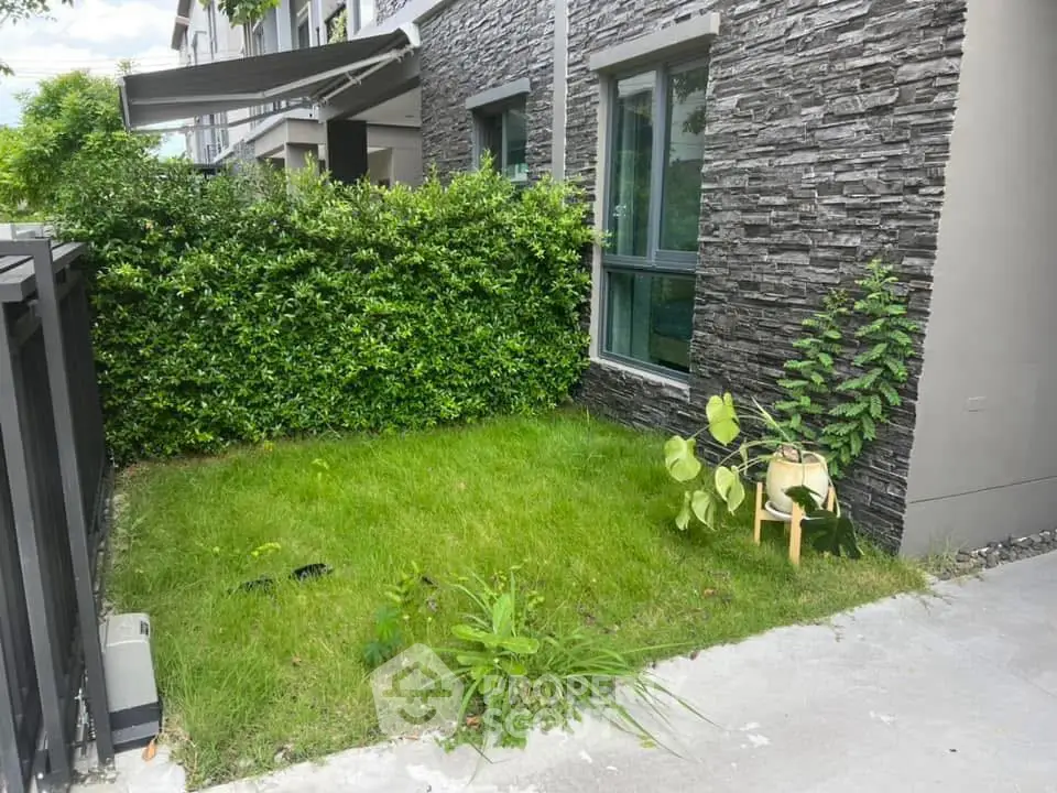 Charming small garden with lush greenery and modern stone facade, perfect for relaxation and outdoor enjoyment.