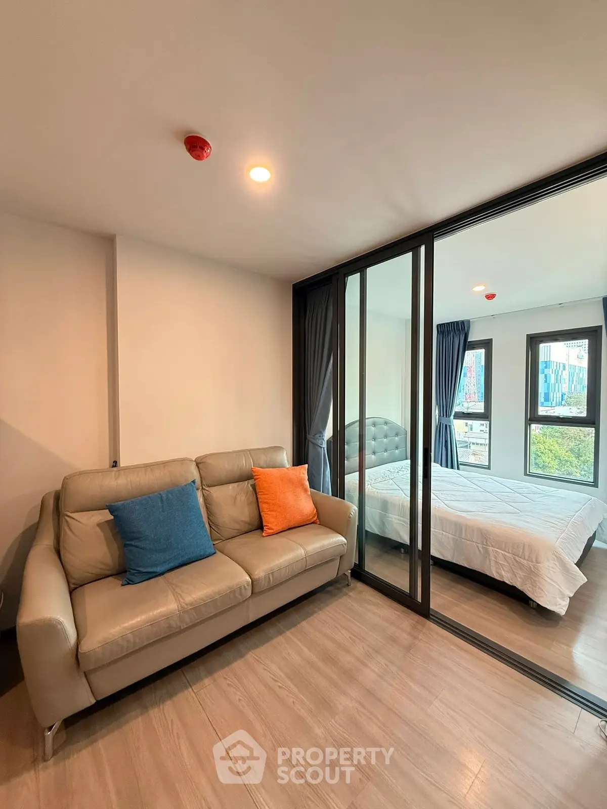 Modern apartment with glass partition separating cozy living room and bright bedroom.