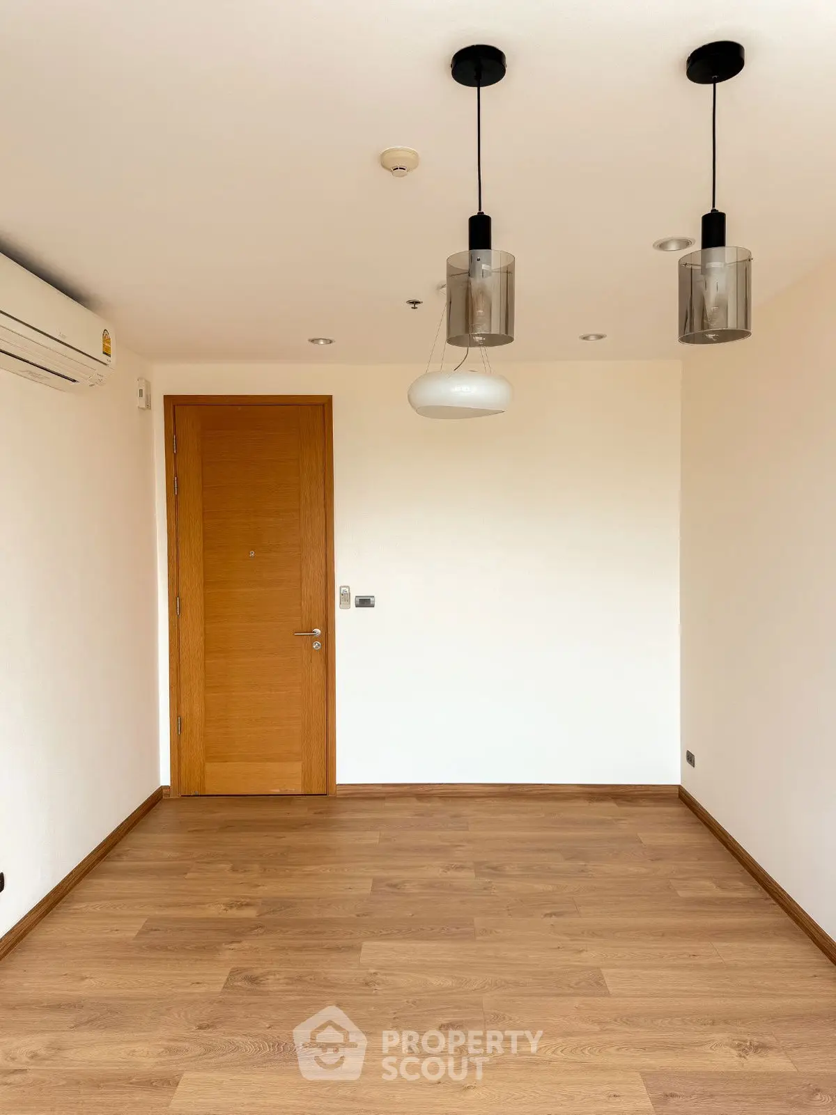 Spacious empty room with wooden flooring and modern lighting fixtures