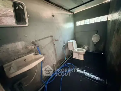 Basic bathroom with toilet, sink, and urinal in a rustic setting.