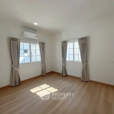 Bright empty room with wooden flooring and large windows, perfect for customization.
