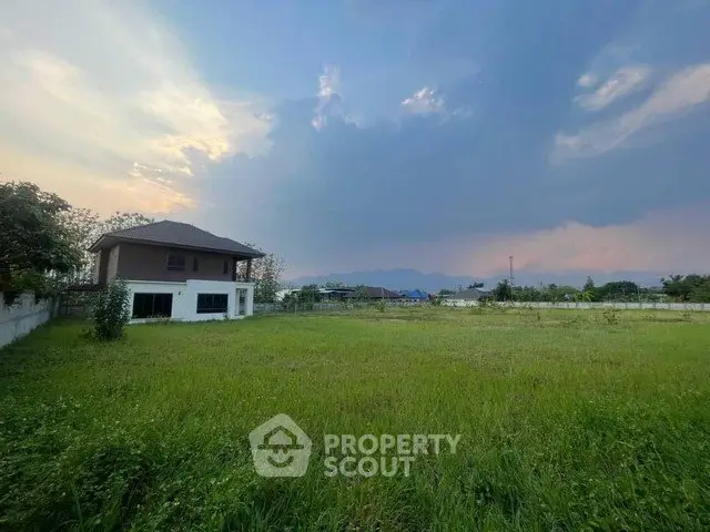 Expansive green field with a distant house under a dramatic sky, perfect for development.