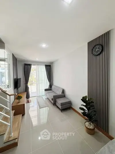Modern living room with sleek design, featuring a cozy gray sofa, stylish decor, and natural light from large windows.