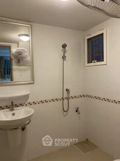 Simple bathroom with shower and sink, featuring white tiles and a small window.