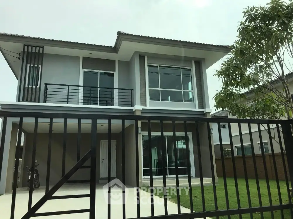 Modern two-story house with large windows and gated entrance in suburban neighborhood.