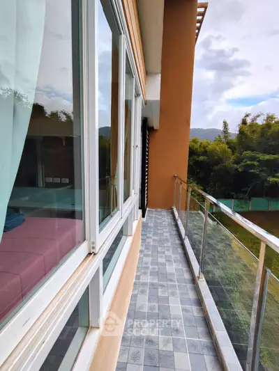 Spacious balcony with glass railing and scenic view of lush greenery, perfect for relaxation.
