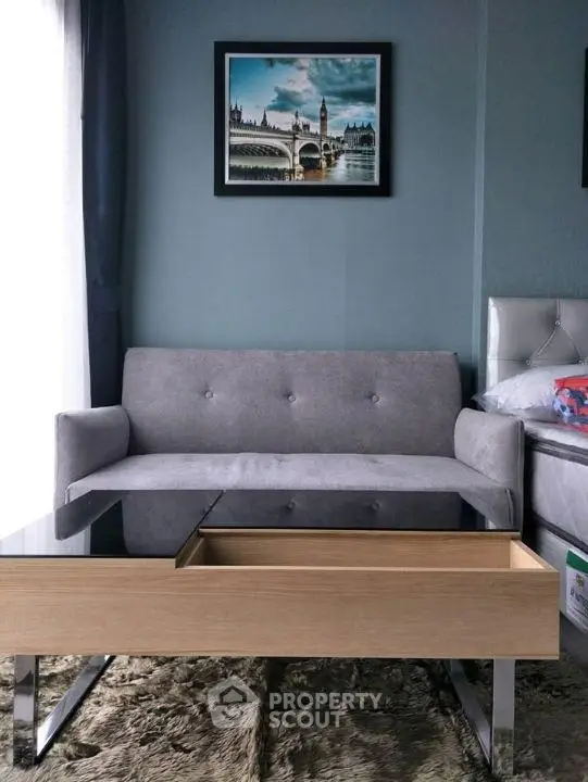 Modern living room with stylish gray sofa and glass-top coffee table, featuring elegant wall art.