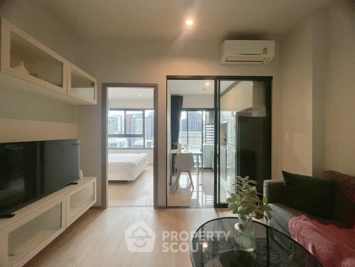 Modern apartment with open living room and bedroom view, featuring sleek furniture and cityscape backdrop.
