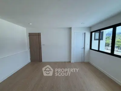 Spacious unfurnished room with large window and wooden flooring, ideal for customization.