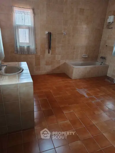 Spacious bathroom with bathtub and tiled flooring, featuring a window for natural light.