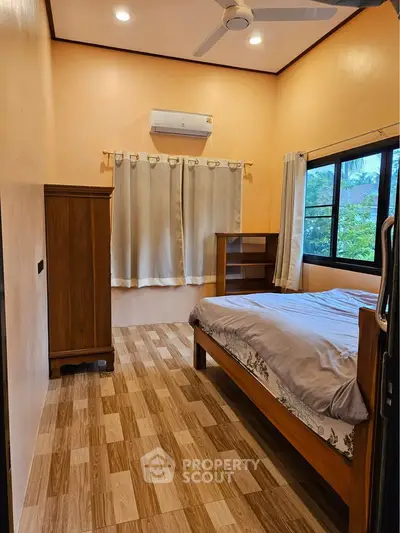 Cozy bedroom with wooden furniture and large window offering natural light.
